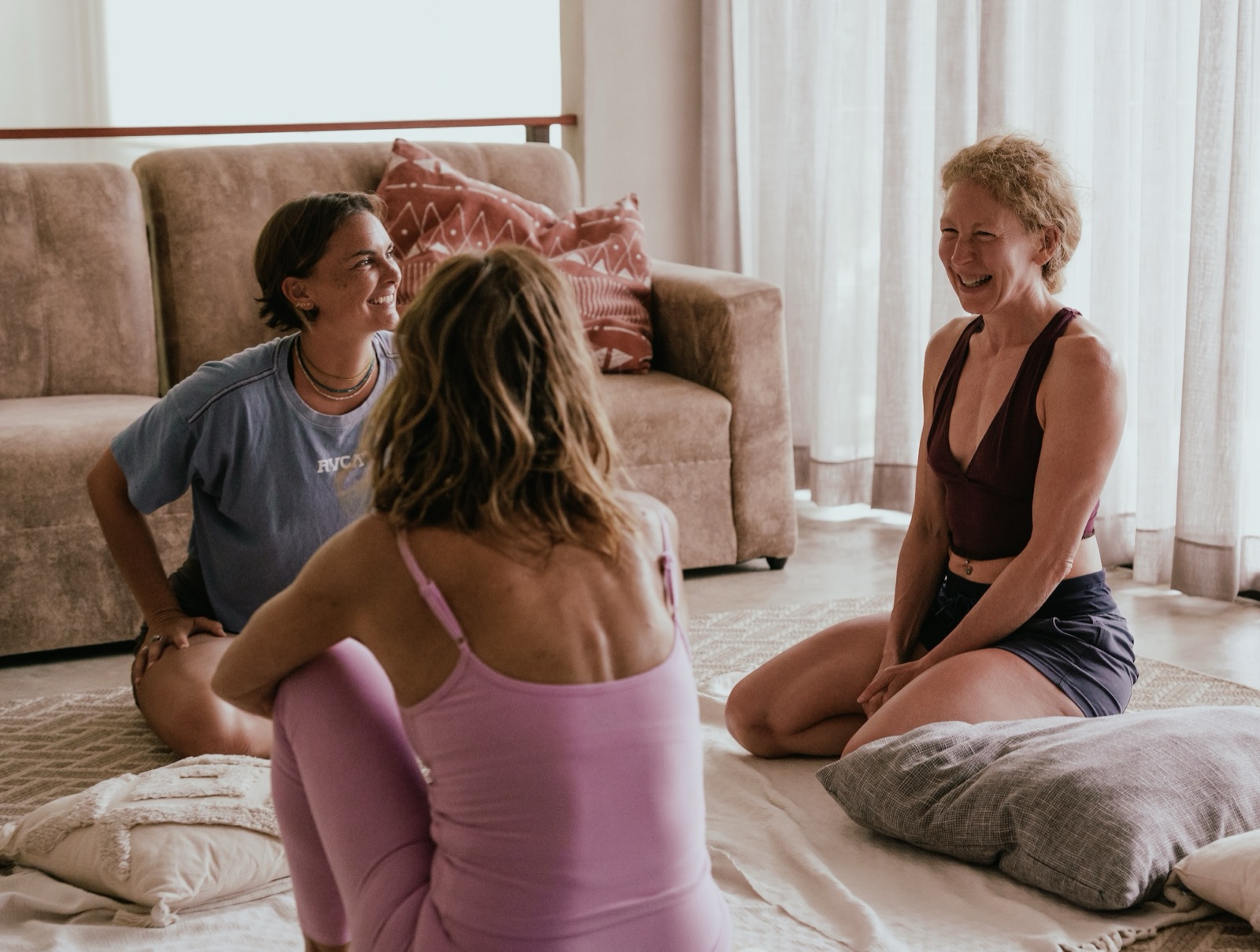 Three women laughing together in a circle on the living room floor