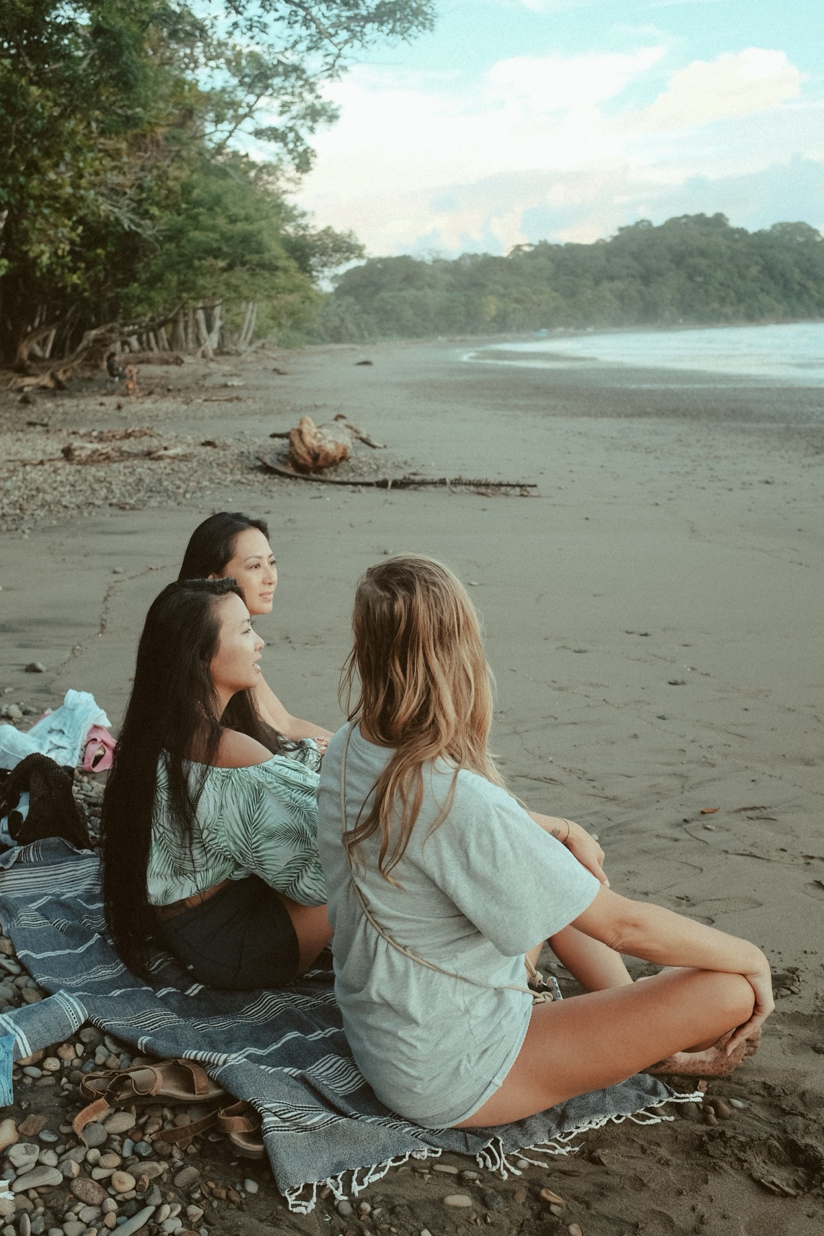 Three women sitting together on a quiet beach at golden hour