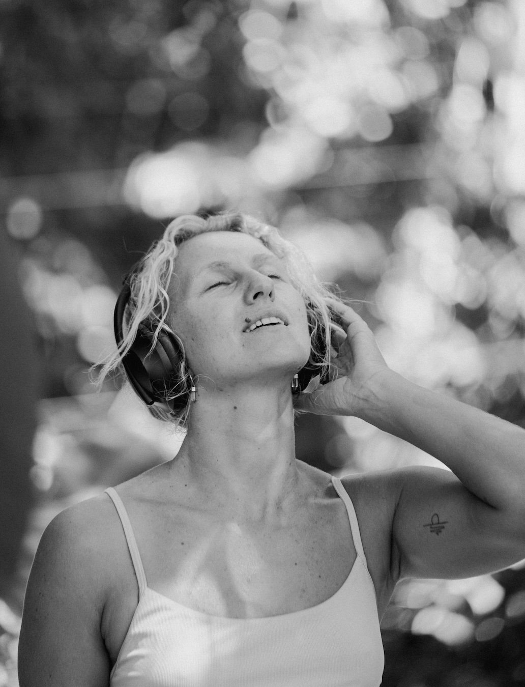 A woman outside with headphones on, eyes closed, listening